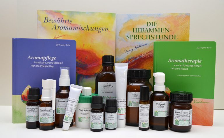 Vor vier deutschsprachigen Büchern zum Thema Aromatherapie und Geburtshilfe sind verschiedene Flaschen, Tuben und Behälter mit Aromatherapieprodukten der Laurentius Apotheke Imst / Pitztal Apotheke angeordnet.