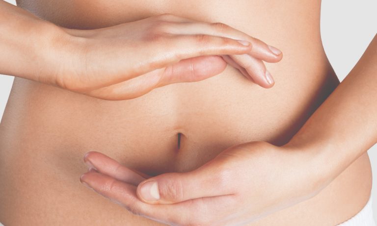 Nahaufnahme des nackten Bauches einer Person, wobei zwei Hände den Bauchnabel einrahmen – eine oberhalb und eine unterhalb –, vor einem einfarbigen Hintergrund. Laurentius Apotheke Imst / Pitztal Apotheke.
