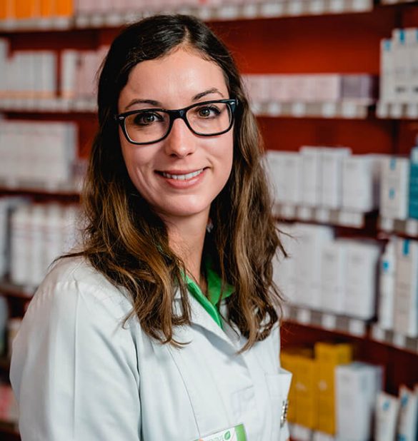 In der Laurentius Apotheke Imst / Pitztal Apotheke steht eine Frau in einem weißen Laborkittel und mit Brille vor den Regalen, die mit Medikamentenschachteln gefüllt sind.
